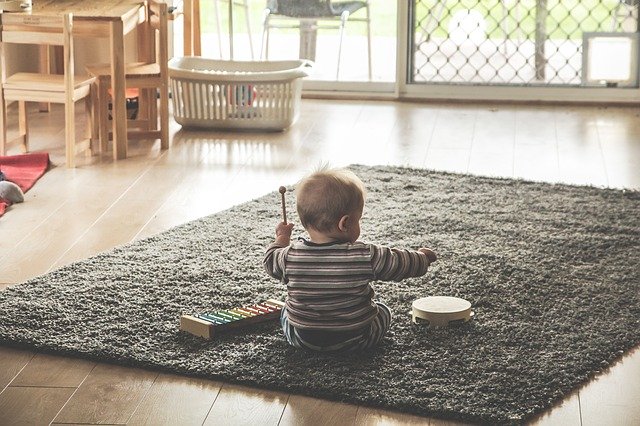 małe dziecko siedzące na dywanie i grające na cymbałakch i bębenku